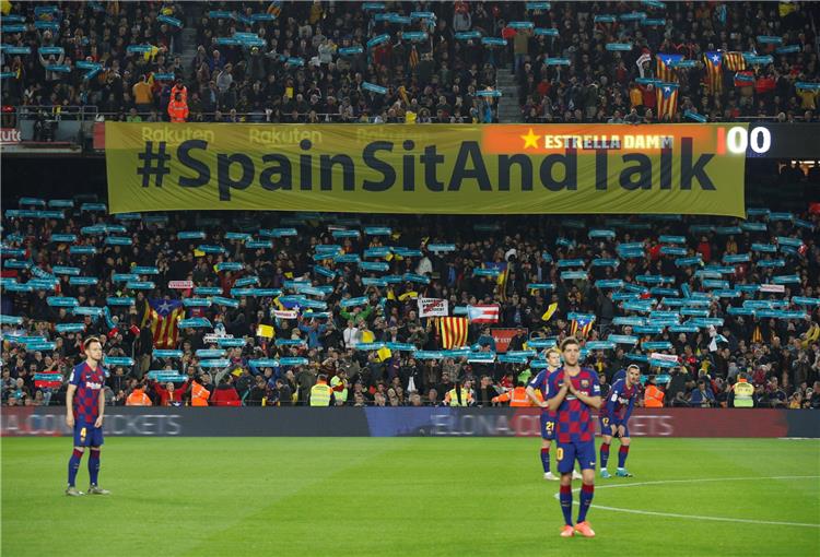 لاعبو برشلونة خلال المباراة ومن خلفهم شعارات تسونامي السياسية
